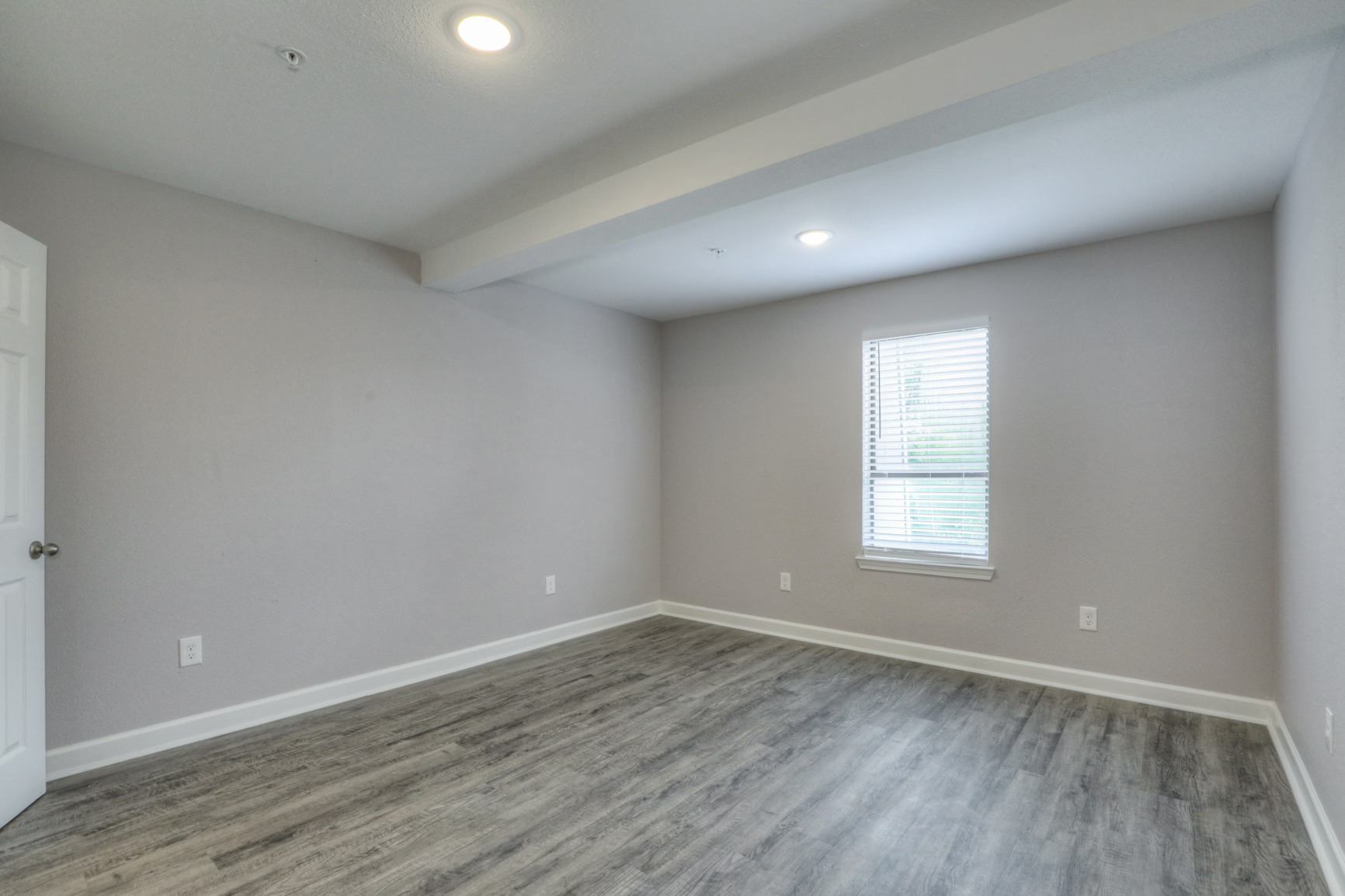 A room with a wooden floor and a window with blinds.